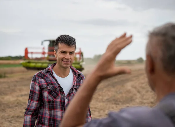 两个农民站在大豆地里 一边聊天 一边把收割者和背景中的收获者结合起来 — 图库照片