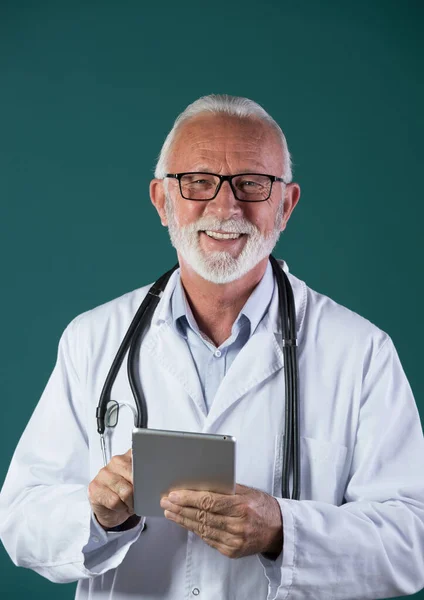 青い背景を背景に 首周りの聴診器 タブレットを保持し 笑顔とカメラを見て 白いコートを身に着けている上級医師の肖像画 — ストック写真