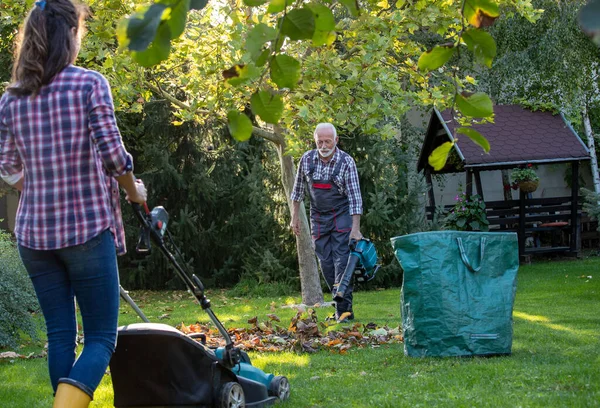 秋天女儿在草坪上割草时 老年人在花园与吹叶机一起干活 — 图库照片