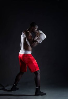 Koyu tenli, üstsüz, eldivenli, gri arka planlı genç bir adam stüdyoda.