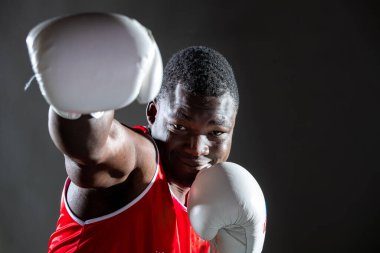 Koyu tenli, üstsüz, eldivenli, gri arka planlı genç bir adam stüdyoda.