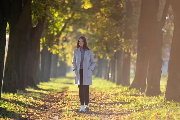 秋の日没時に公園を歩くコート姿の若い女性 — ストック写真