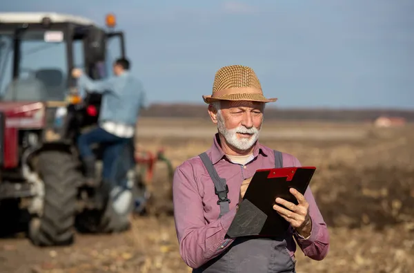 Landwirt Schreibt Notizen Notizblock Auf Feld Mit Traktor Hintergrund — Stockfoto