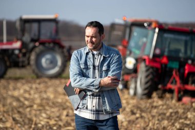 Mid adult farm worker standing on agricultural field with crossed arms and thinking of something.