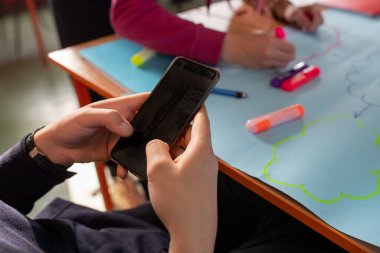 Close up of student holding mobile phone while other team members working on presentation on workshop