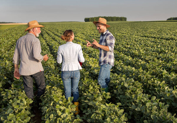 Happy farmers communicating with female insurance agent while walking through cultivated land.