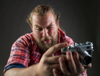 Young bearded man making funny facial expression while taking a photo with old-fashioned camera.