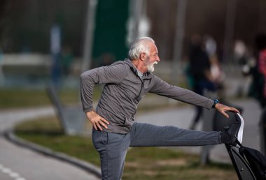 Spor salonundaki antrenmandan sonra eşofmanlı yaşlı sakallı adam esniyor.