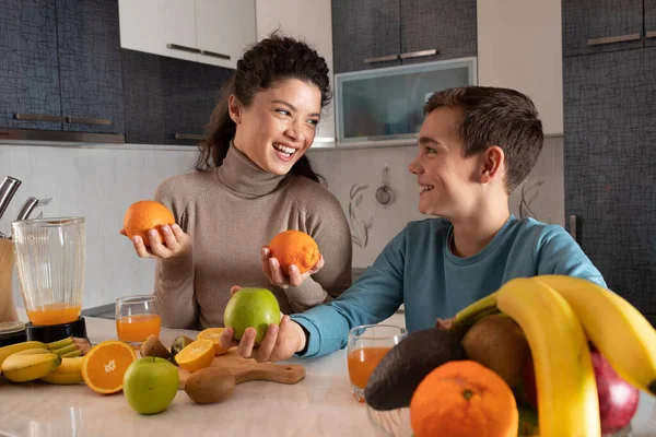 美丽快乐的妈妈和她的儿子在厨房里用新鲜的水果准备果汁 — 图库照片