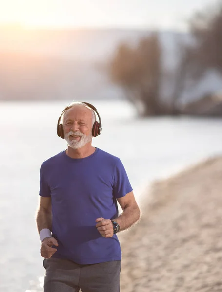 Senior Muž Fitness Oblečení Běží Sluchátky Podél Pláže — Stock fotografie