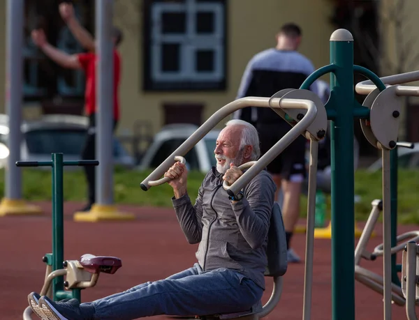 Oudere Man Een Trainingspak Doet Krachttraining Een Openbare Fitnessruimte Machine — Stockfoto