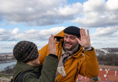 Gülümseyen baba ve küçük oğlu, soğuk kış zamanı dışarıda ceketleriyle dikilirken birbirlerine beşlik çakıyorlar..