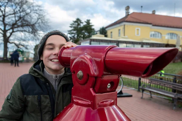 不思議な笑顔の少年が公共の望遠鏡を通して街を観察します — ストック写真