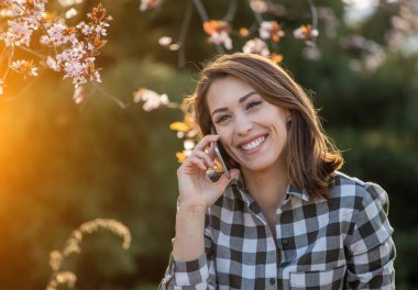 Bir bahar sabahı açık havada yürürken telefonda konuşan güzel bir kadının portresi..