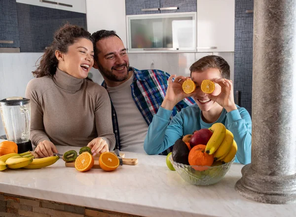 妈妈和爸爸站在厨房里笑着他们的儿子 他们的儿子一边鬼鬼祟祟 一边用橙色的薄片蒙住眼睛 — 图库照片