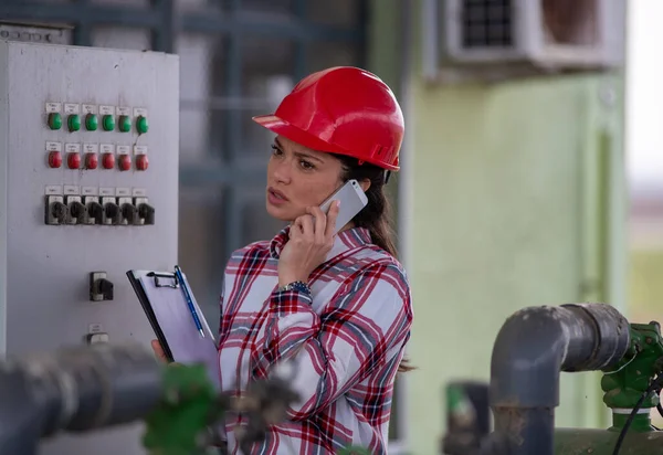 室外农机厂里忙碌的女工程师 戴着头盔 拿着文件在电猪前打电话 — 图库照片