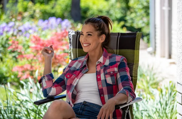 Güzel, genç, gülümseyen bir kadın bahçede bir sandalyede oturuyor ve güzel, güneşli bir günün tadını çıkarıyor..