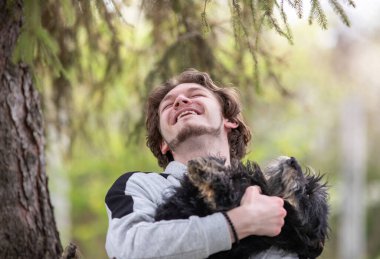 Mutlu genç adam kucağında sevimli bir köpek, oynuyor, sarılıyor ve gülüyor, parkta.