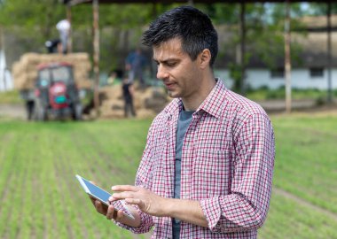 Çiftlikte tablet üzerinde çalışan, düz gömlekli yakışıklı bir çiftçinin portresi.
