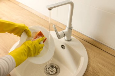 Top view of female hands with protective gloves washing dishes under tap water in sink