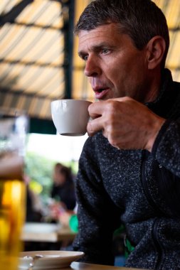 Kafede kahve içen ciddi bir olgun adamın portresi ve endişeli görünüyor.