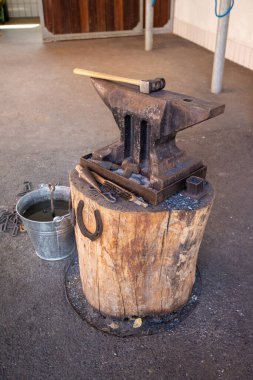 Close up of hammer on anvil in forge with horseshoes 