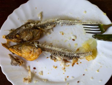 Taze kızarmış alabalıkların lezzetli yemeklerinden kafaları olan balık kemikleriyle dolu tabağın üst görüntüsü. 