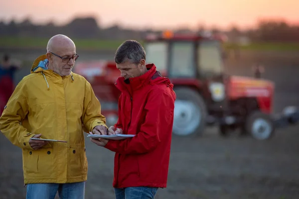 秋の日没にトラクターの前で畑で話している2人の上級農家 — ストック写真