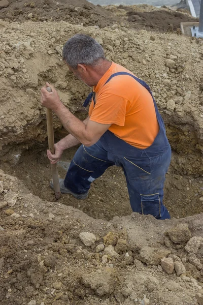 Worker with a shovel looking for lost manhole after working exca — Stock Photo, Image