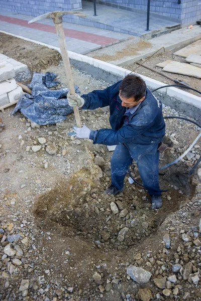 Trabajador de la construcción cavando un agujero subterráneo profundo con una selección —  Fotos de Stock