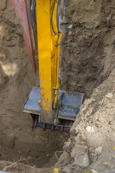 Excavator arm digging deep hole seeking cracked sewage pipe — Stock Photo, Image