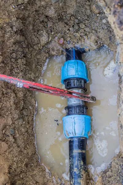 Broken pvc pipe in trench with wrench leaks water 2 — Stock Photo, Image