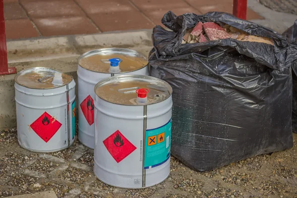 Cans of industrial chemical with flammable sign and bag of waste — Stock Photo, Image