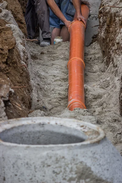 Trabajadores colocando tubos de PVC en el fondo de la zanja — Foto de Stock