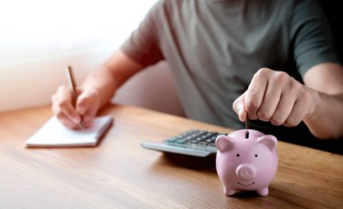 Para biriktirmek için pembe kumbaraya bozuk para koyan bir adamın yakın plan resmi. Planlama aşaması, gelecek için para biriktirme, emeklilik fonu. Yatırım finansmanı muhasebe kavramı.