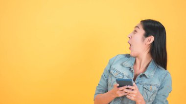 20 'li yaşlardaki güzel ve şaşkın Asyalı kadın izole edilmiş stüdyo sarı arka planda cep telefonu kullanıyor. Heyecan verici bir gülümseme ve mutlu bir şirinlik başarıyı müjdeler..