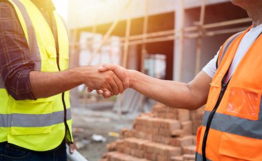 El sıkışma, profesyonel inşaat mühendisi ya da inşaatçı, ustabaşı olan mimar. Başarı, inşaat projesini karşılarken ve inşaat alanında el sıkışarak işaret ederken.