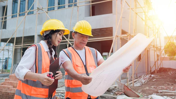 Asian woman civil engineer or Architect, inspector with contractor, foreman or worker wear safety helmet. Colleagues discussing, meeting about construction building project on site.