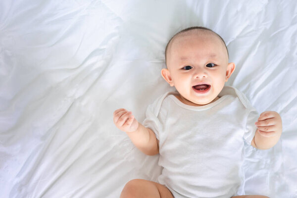Portrait of cute asian newborn baby lying play on white bed look at camera with laughing smile happy face. Innocent little new infant adorable. Parenthood and Mother Day concept.