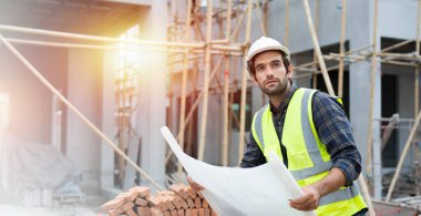 Profesyonel inşaat mühendisi ya da mimar güvenlik kaskı takıyor. Yakışıklı mühendis çalışırken, bina inşaatı projesinin planlarını kontrol ediyor. Emlak kavramı.