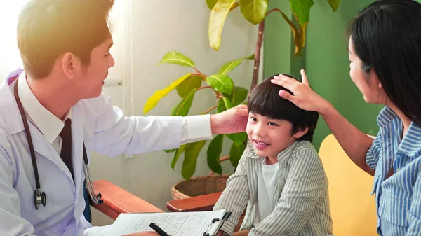 Asian male pediatrician talking exam with child boy patient visit doctor and young asian mother. Professional, Consulting pediatric health checkup in clinic office. Medical health care concept.