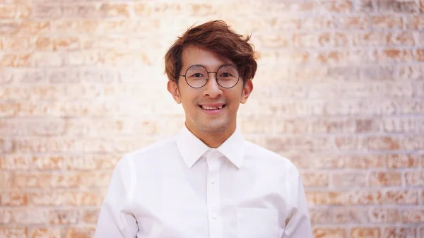 Portrait of Smiling Asian businessman in glasses standing in white shirt wear looking at camera and smiling in modern office workplace.