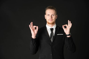 Siyah takım elbiseli yakışıklı iş adamının portresi siyah arka planda izole edilmiş sembol eli gösteriyor.