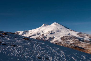 Kafkasya 'nın inanılmaz karlı dağ manzarası, açık mavi gökyüzünde Elbrus Dağı' nın zirveleri.