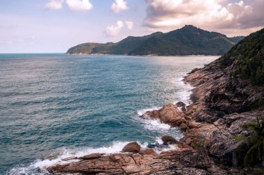 Vahşi bir yer, taştan bir sahil, üst manzara, gün batımında turkuaz deniz dalgaları.
