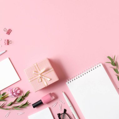 Pembe arka planda not defteri, kalem, hediye ve diğer aksesuarlara sahip işyeri