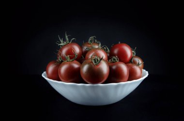 Beautiful tomatoes in a white plate on a black background. Cumato tomatoes.