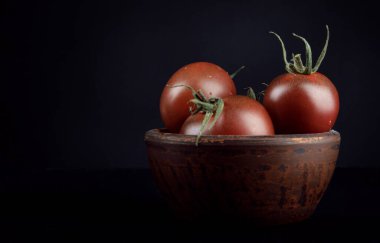 Ripe tomatoes in a plate on a black background. Cumato tomatoes.