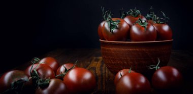 Ripe juicy tomatoes in a clay plate and next to it on a black background.