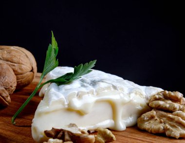A piece of camembert cheese and walnut lie on a wooden board. Camembert cheese with white noble mold.